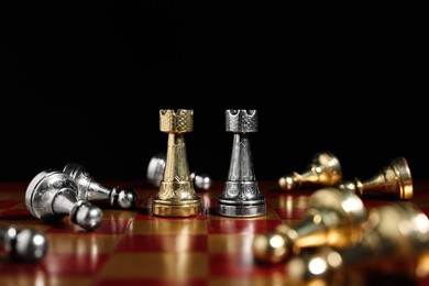 Photo of Golden and silver rooks among fallen pieces on chessboard against black background, closeup. Competition concept