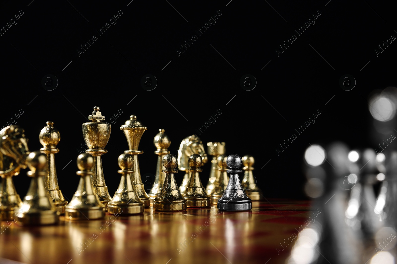 Photo of Silver pawn in front of golden chess pieces on chessboard against black background, closeup. Competition concept