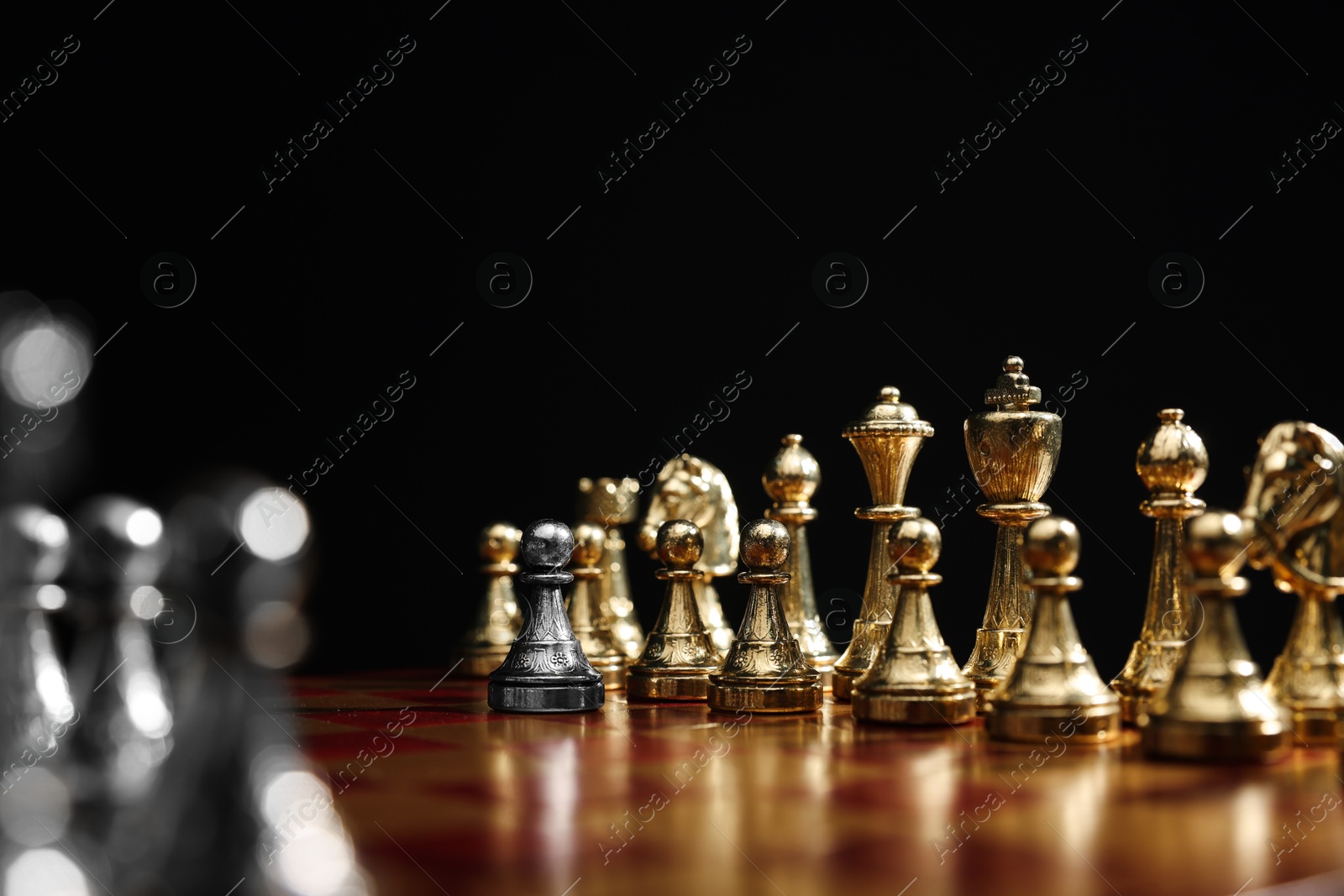 Photo of Silver pawn in front of golden chess pieces on chessboard against black background, closeup. Competition concept