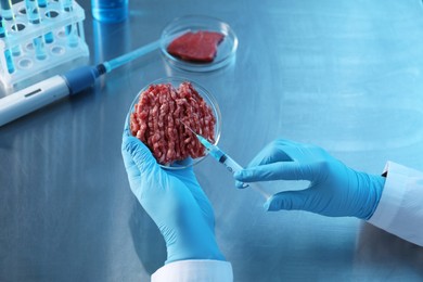 Photo of GMO concept. Scientist injecting something into minced meat at table, closeup