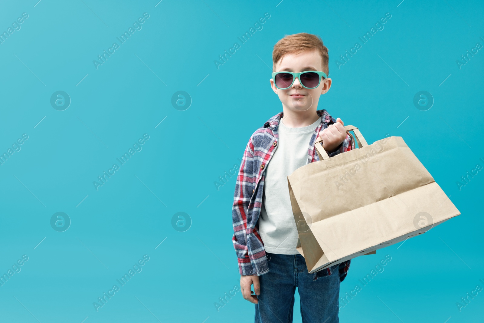 Photo of Cute little boy with shopping bags on light blue background. Space for text