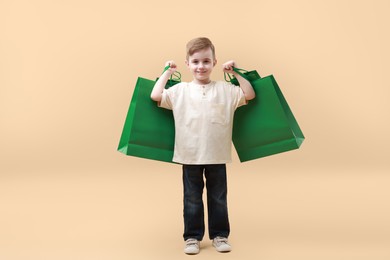 Photo of Cute little boy with shopping bags on beige background