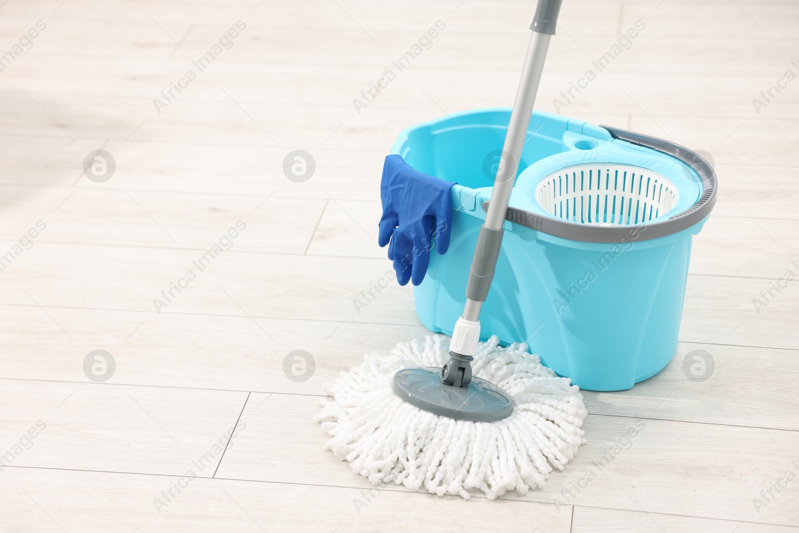 Photo of String mop, bucket and glove on floor indoors, space for text