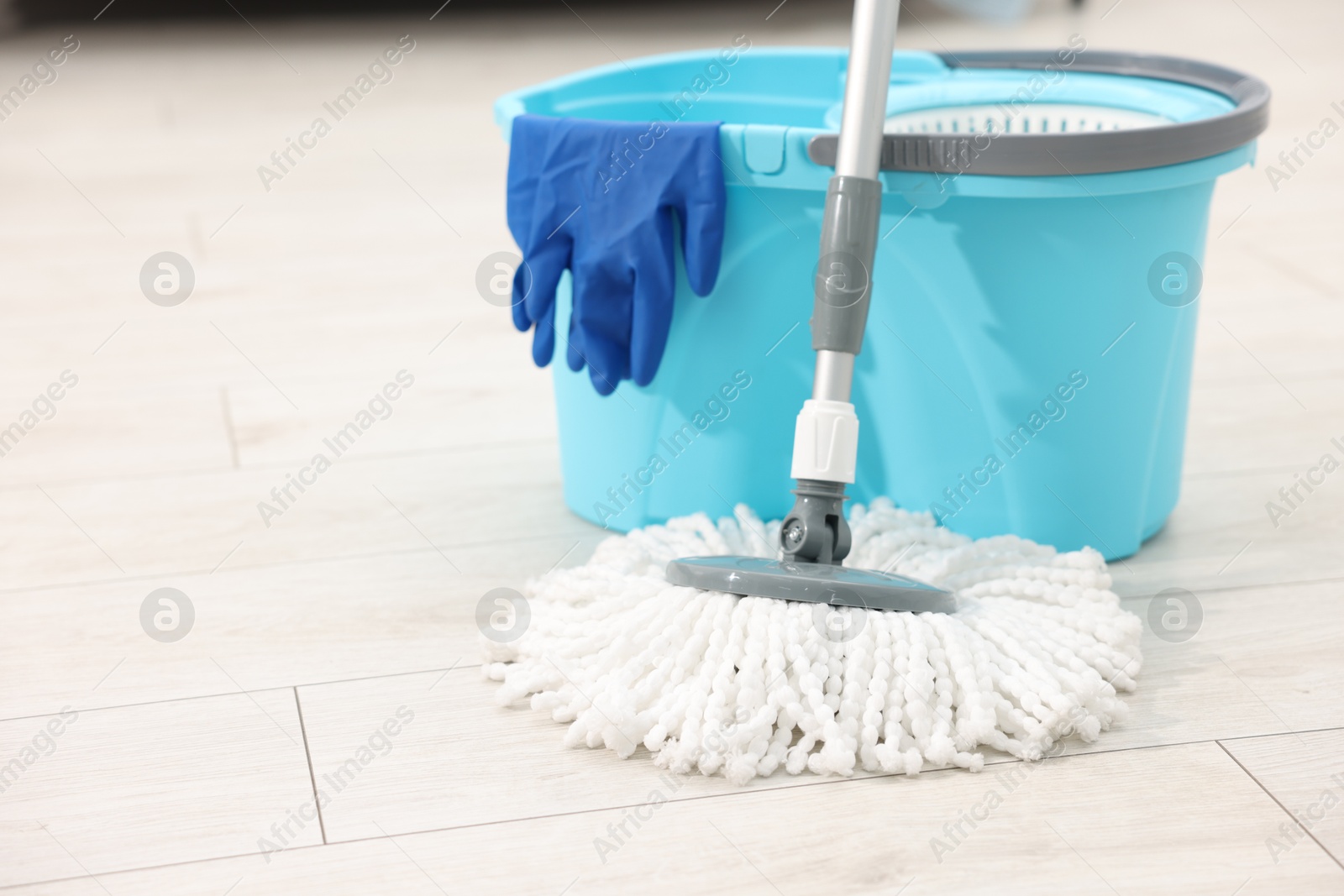 Photo of String mop, bucket and glove on floor indoors, space for text