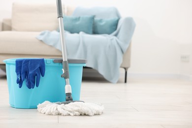 Photo of String mop, bucket and gloves on floor indoors, space for text