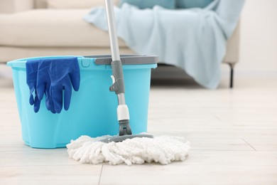 Photo of String mop, bucket and gloves on floor indoors, space for text