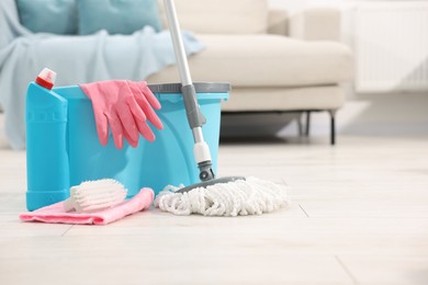 Photo of String mop and bucket with cleaning supplies on wooden floor indoors, space for text