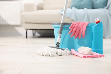 Photo of String mop and bucket with cleaning supplies on wooden floor indoors, space for text