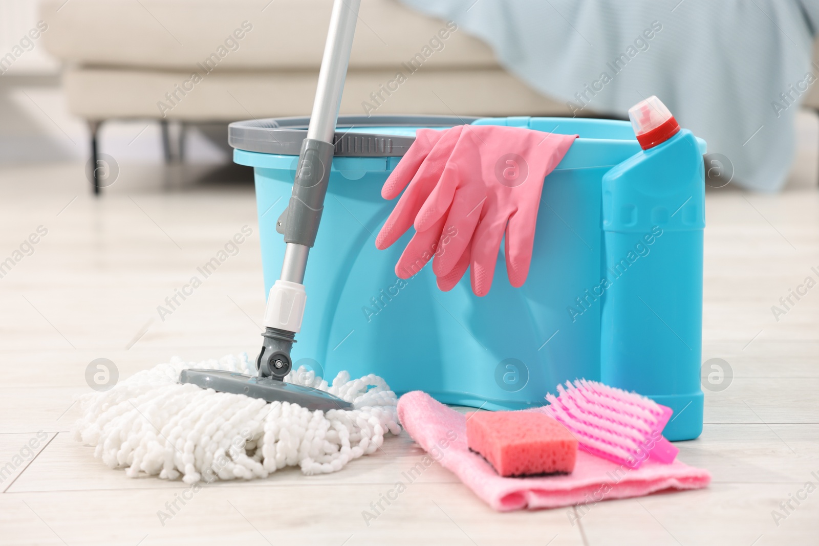 Photo of String mop and bucket with cleaning supplies on wooden floor indoors