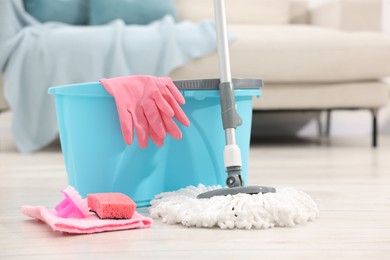 Photo of String mop and bucket with cleaning supplies on wooden floor indoors