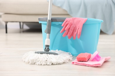 Photo of String mop and bucket with cleaning supplies on wooden floor indoors