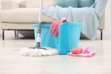 Photo of String mop and bucket with cleaning supplies on wooden floor indoors