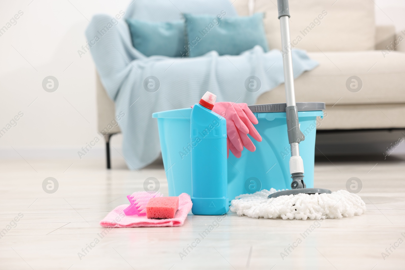 Photo of String mop and bucket with cleaning supplies on wooden floor indoors