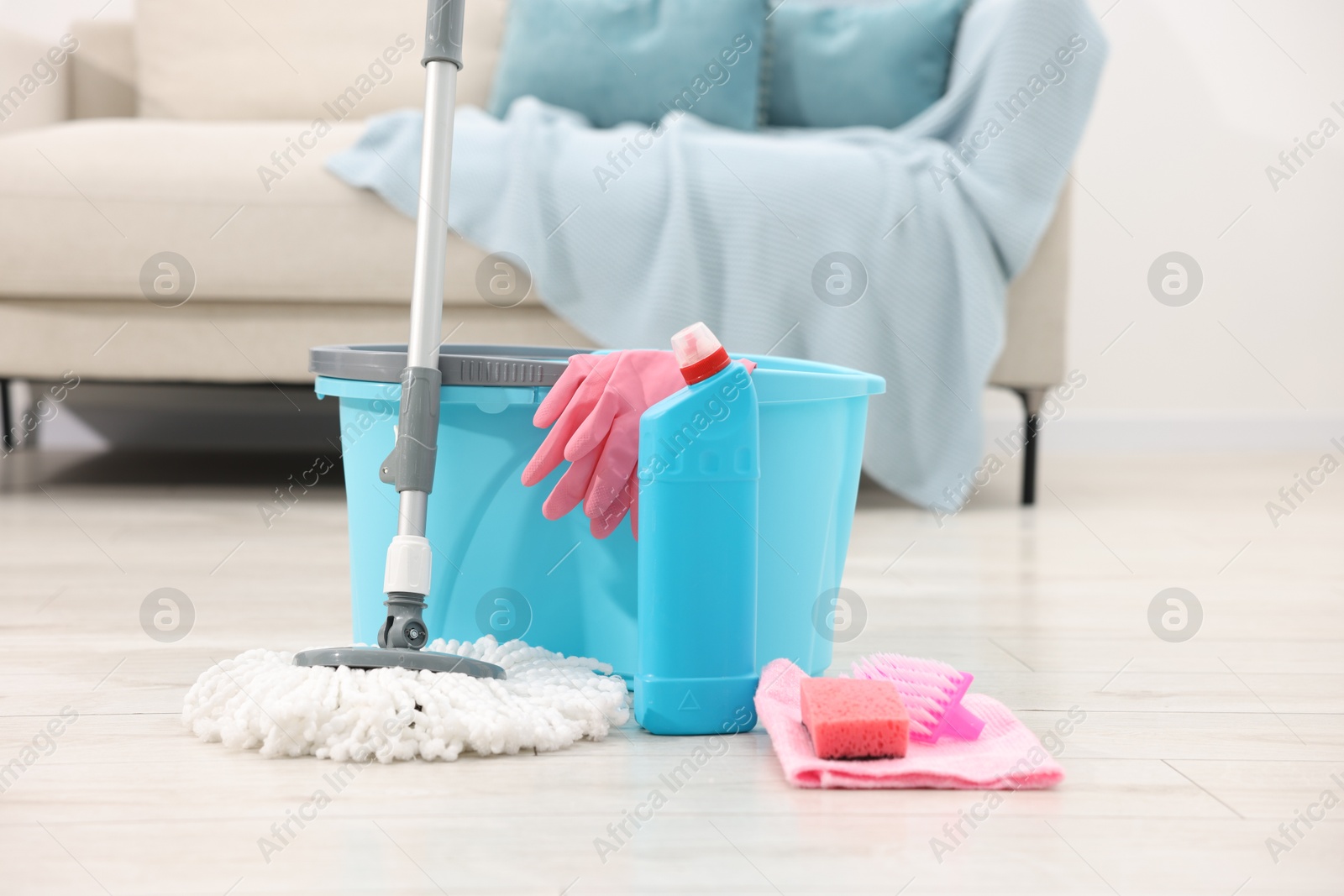 Photo of String mop and bucket with cleaning supplies on wooden floor indoors