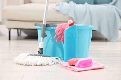 Photo of String mop and bucket with cleaning supplies on wooden floor indoors