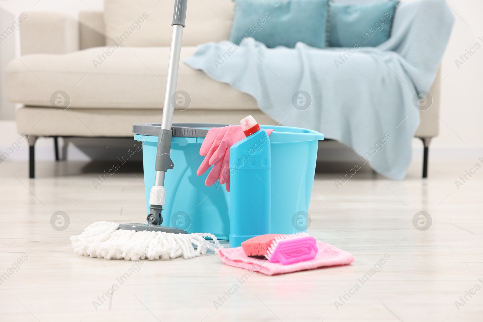 Photo of String mop and bucket with cleaning supplies on wooden floor indoors