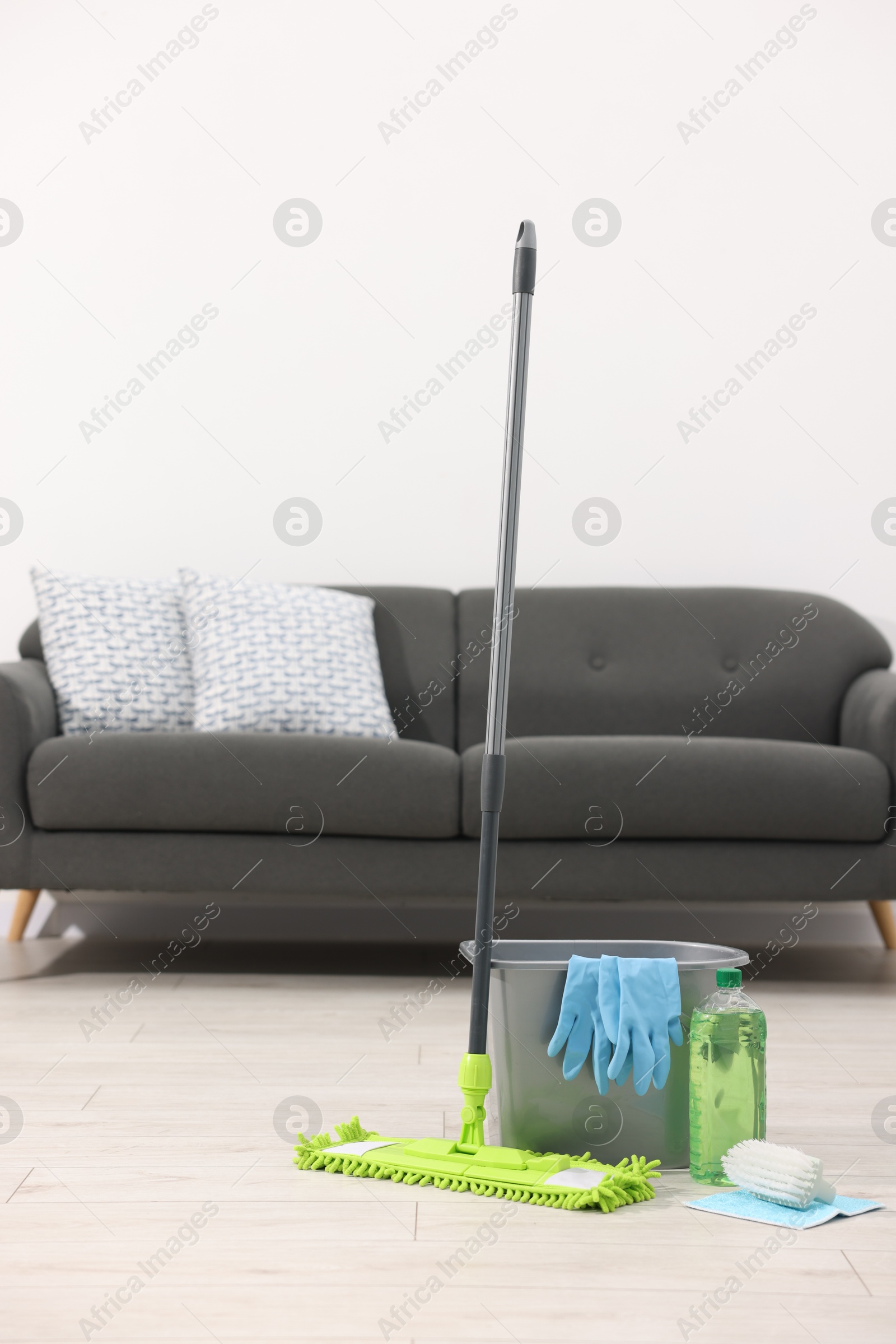 Photo of Microfiber mop and bucket with cleaning supplies on wooden floor indoors