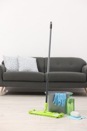 Photo of Microfiber mop and bucket with cleaning supplies on wooden floor indoors