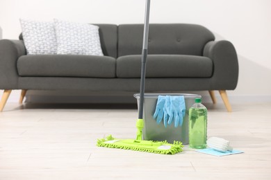 Photo of Microfiber mop and bucket with cleaning supplies on wooden floor indoors, space for text