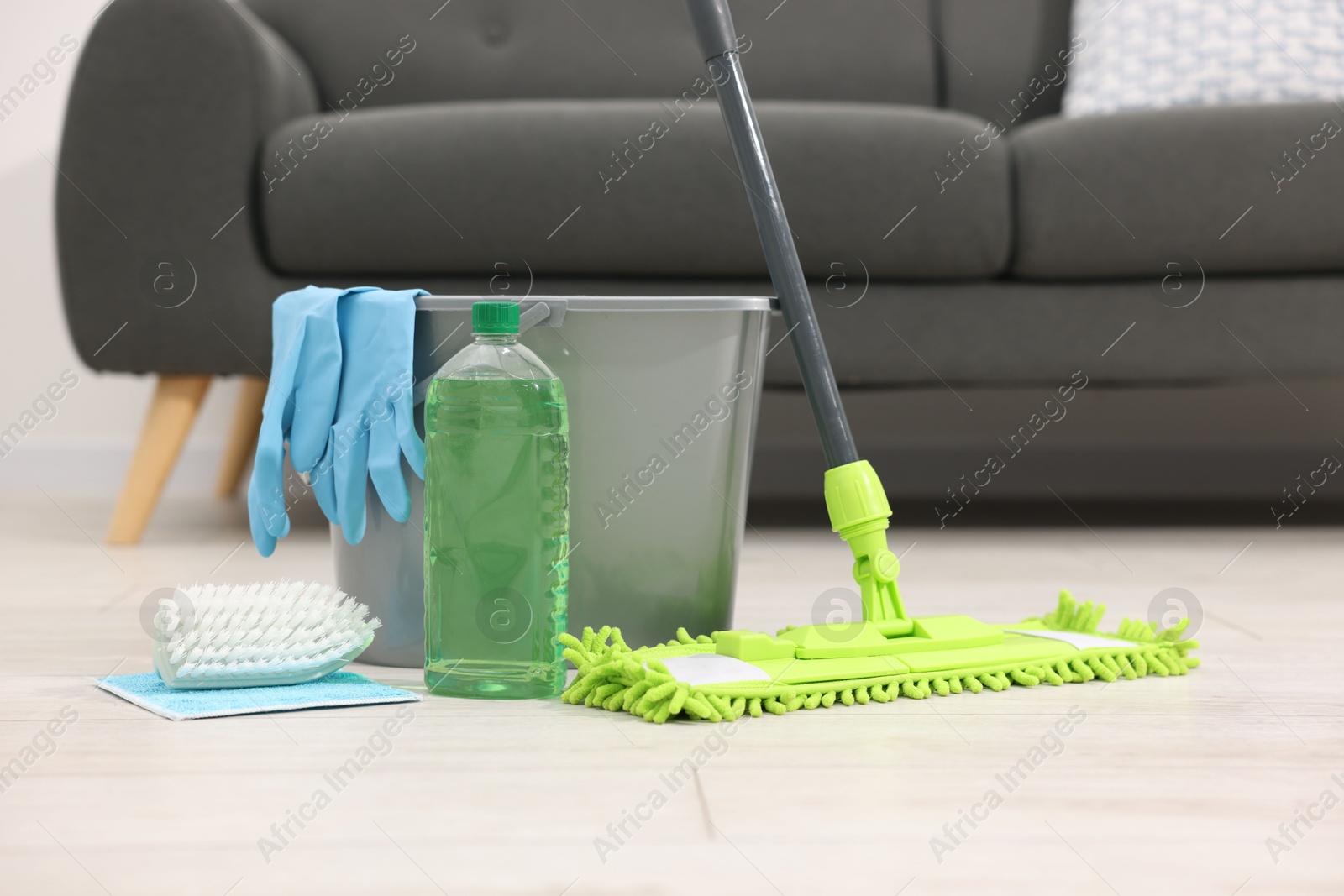 Photo of Microfiber mop and bucket with cleaning supplies on wooden floor indoors