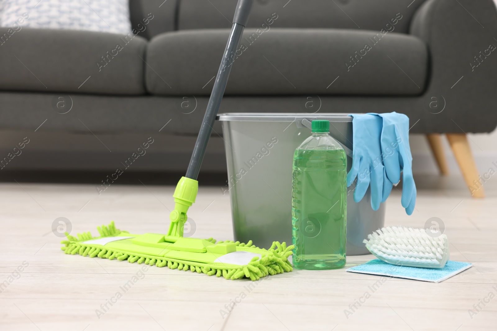 Photo of Microfiber mop and bucket with cleaning supplies on wooden floor indoors