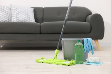 Photo of Microfiber mop and bucket with cleaning supplies on wooden floor indoors