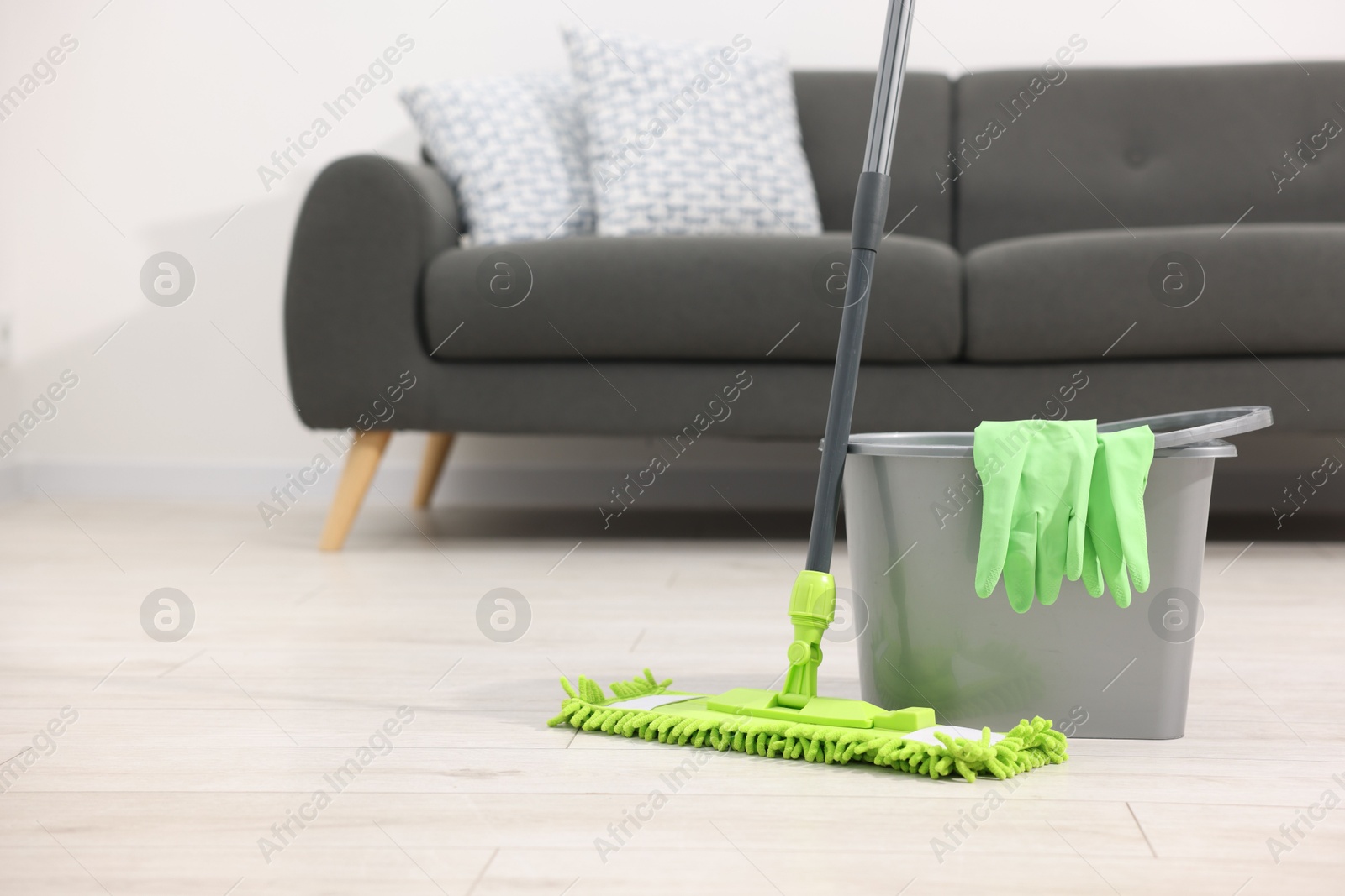 Photo of Microfiber mop, bucket and gloves on floor indoors, space for text