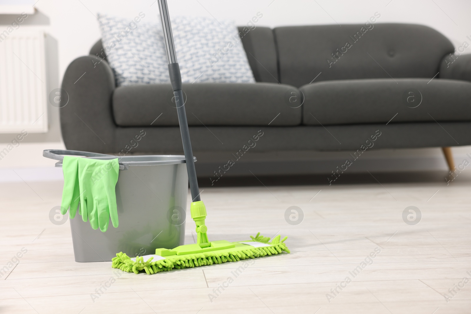 Photo of Microfiber mop, bucket and gloves on floor indoors, space for text