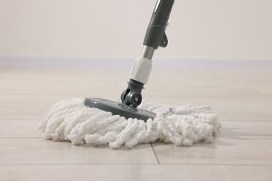 Photo of String mop on wooden floor indoors. Cleaning equipment