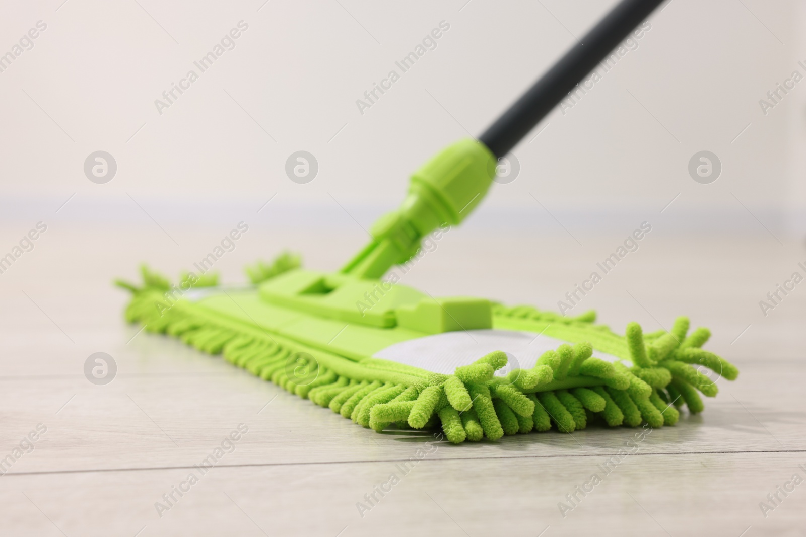 Photo of Microfiber mop on wooden floor indoors, closeup. Cleaning equipment