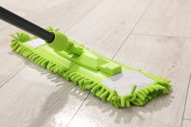 Photo of Microfiber mop on wooden floor, closeup. Cleaning equipment