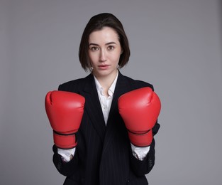 Competition. Businesswoman in suit wearing boxing gloves on grey background