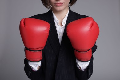 Photo of Competition. Businesswoman in suit wearing boxing gloves on grey background, closeup