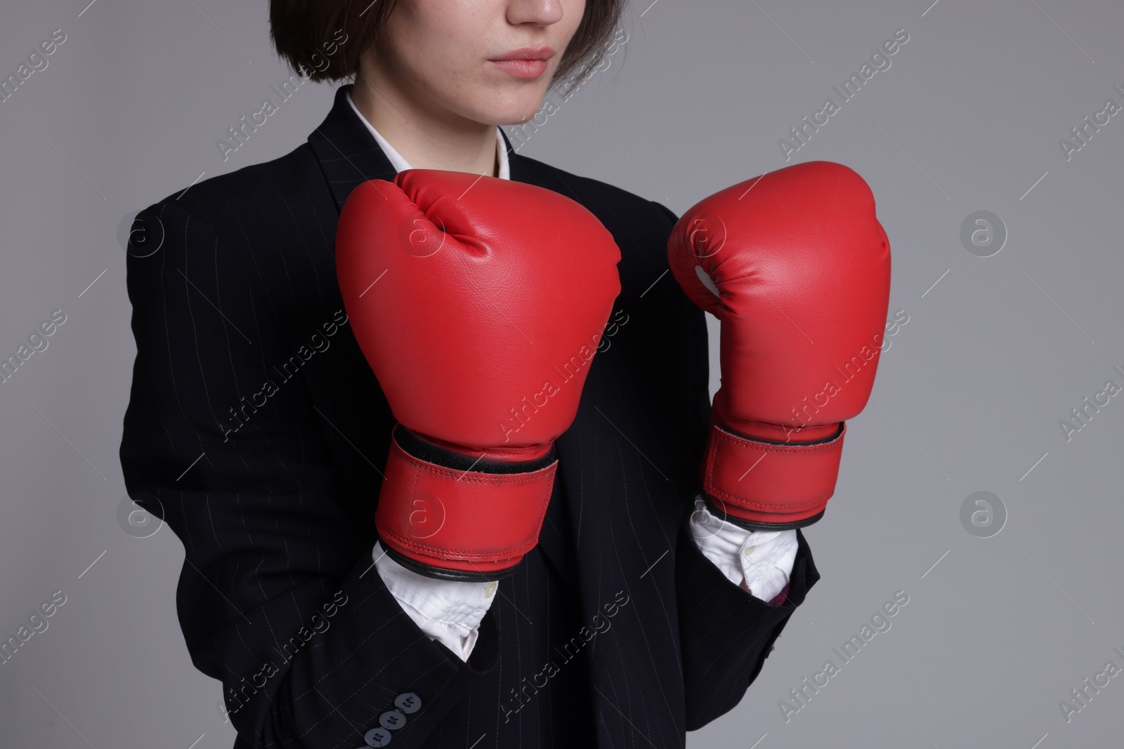 Photo of Competition. Businesswoman in suit wearing boxing gloves on grey background, closeup with space for text