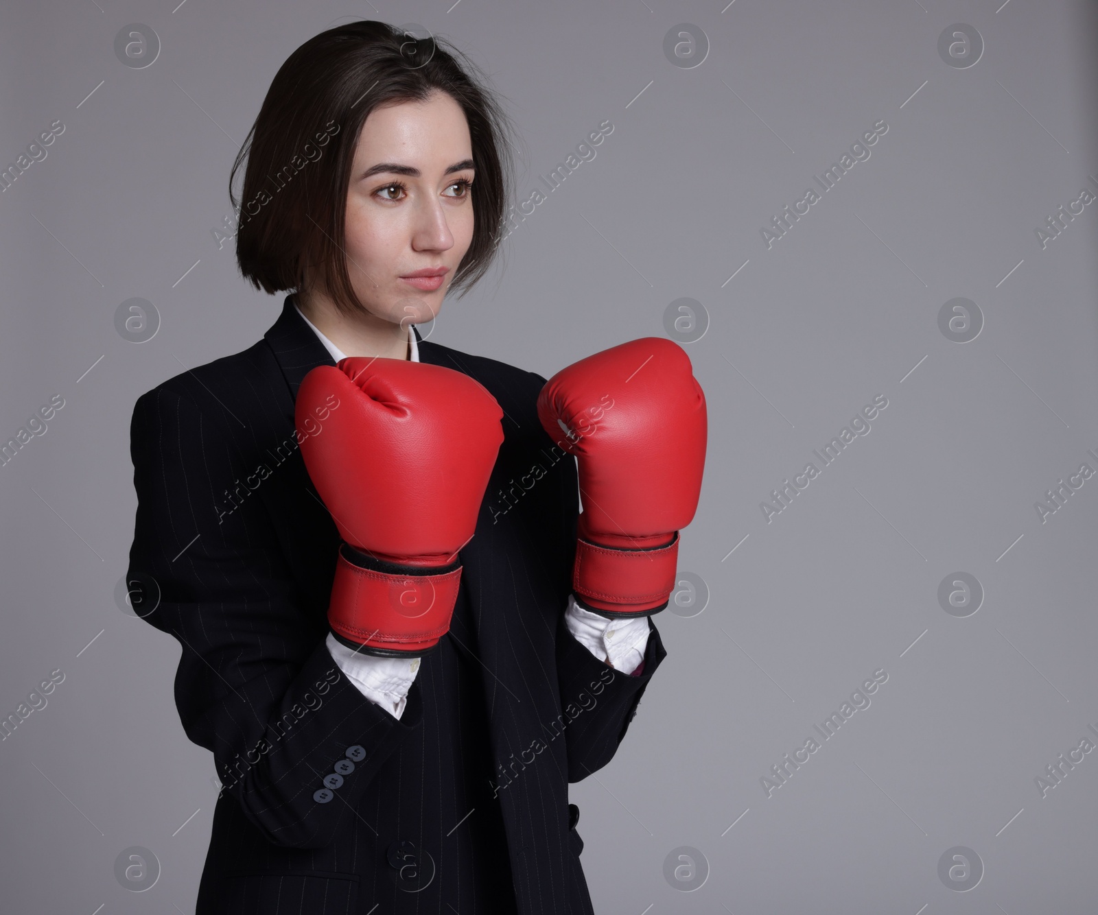 Photo of Competition. Businesswoman in suit wearing boxing gloves on grey background, space for text