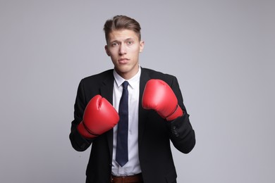 Photo of Competition. Businessman in suit wearing boxing gloves on grey background