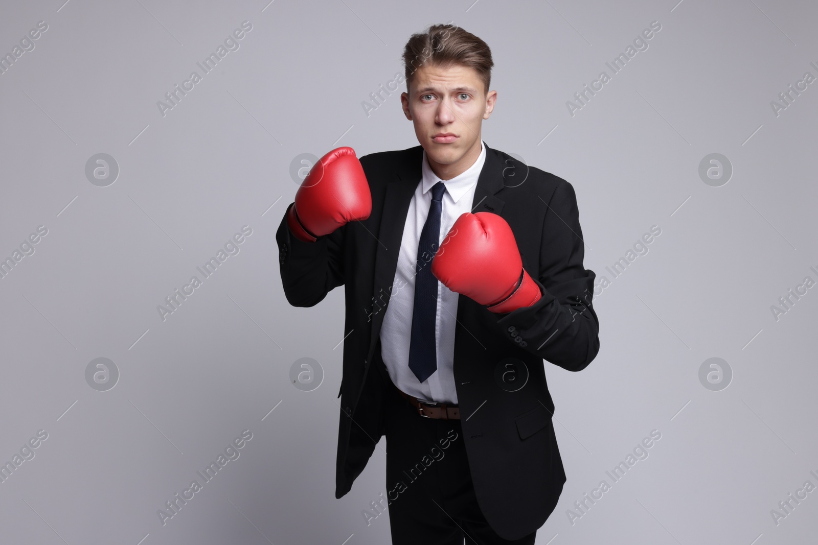 Photo of Competition. Businessman in suit wearing boxing gloves on grey background, space for text