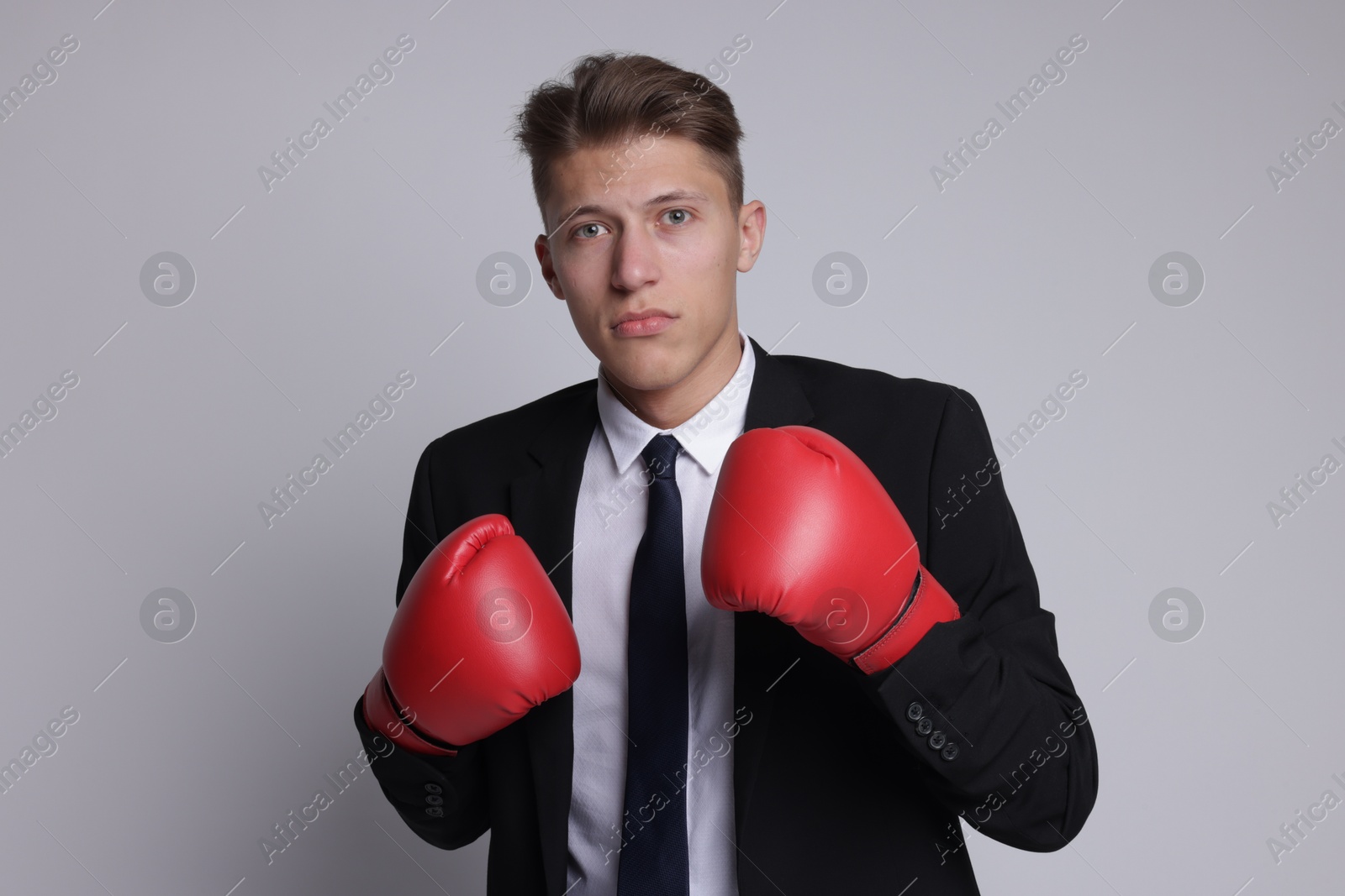 Photo of Competition. Businessman in suit wearing boxing gloves on grey background