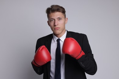 Competition. Businessman in suit wearing boxing gloves on grey background