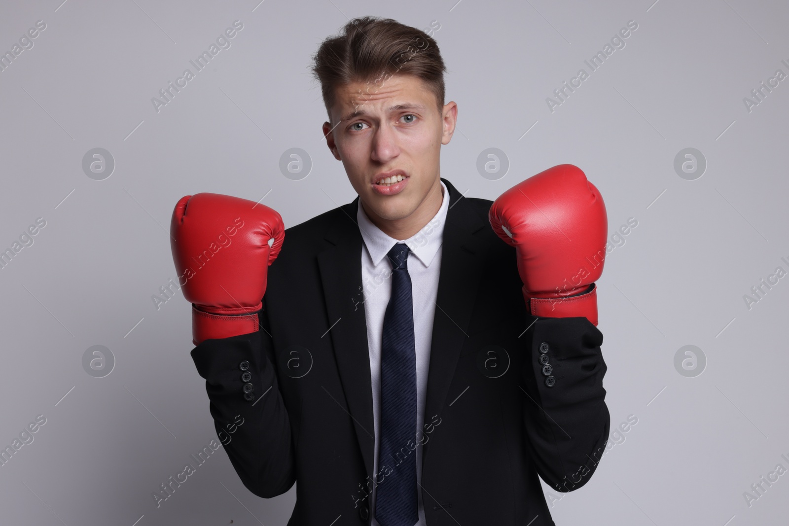 Photo of Competition. Businessman in suit wearing boxing gloves on grey background