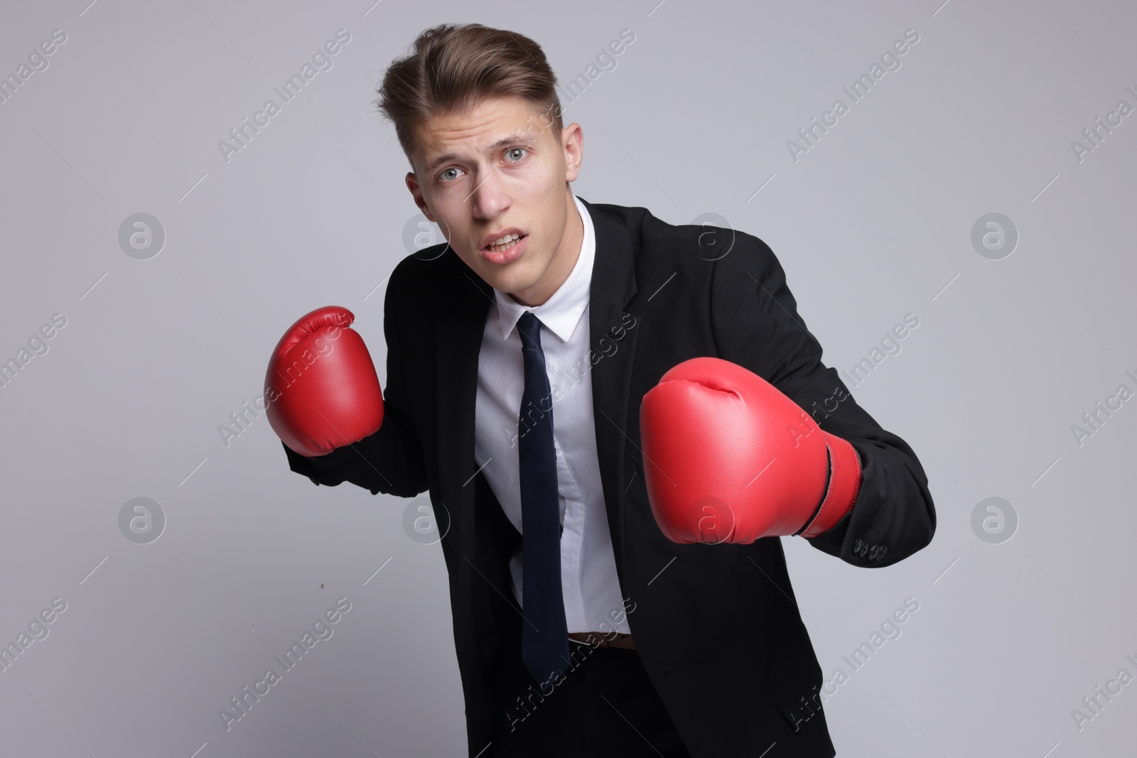 Photo of Competition. Businessman in suit wearing boxing gloves on grey background