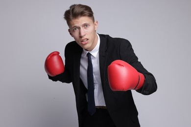 Competition. Businessman in suit wearing boxing gloves on grey background