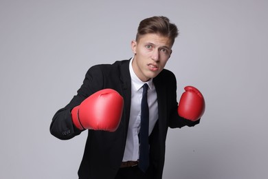 Photo of Competition. Businessman in suit wearing boxing gloves on grey background