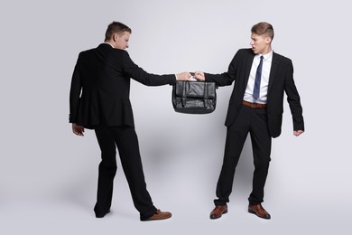 Photo of Competition concept. Businessmen pulling leather briefcase on grey background