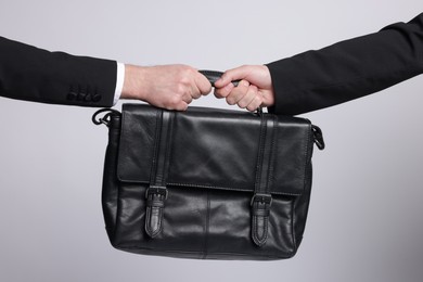 Photo of Competition concept. Businessmen pulling leather briefcase on grey background, closeup