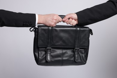 Photo of Competition concept. Businessmen pulling leather briefcase on grey background, closeup