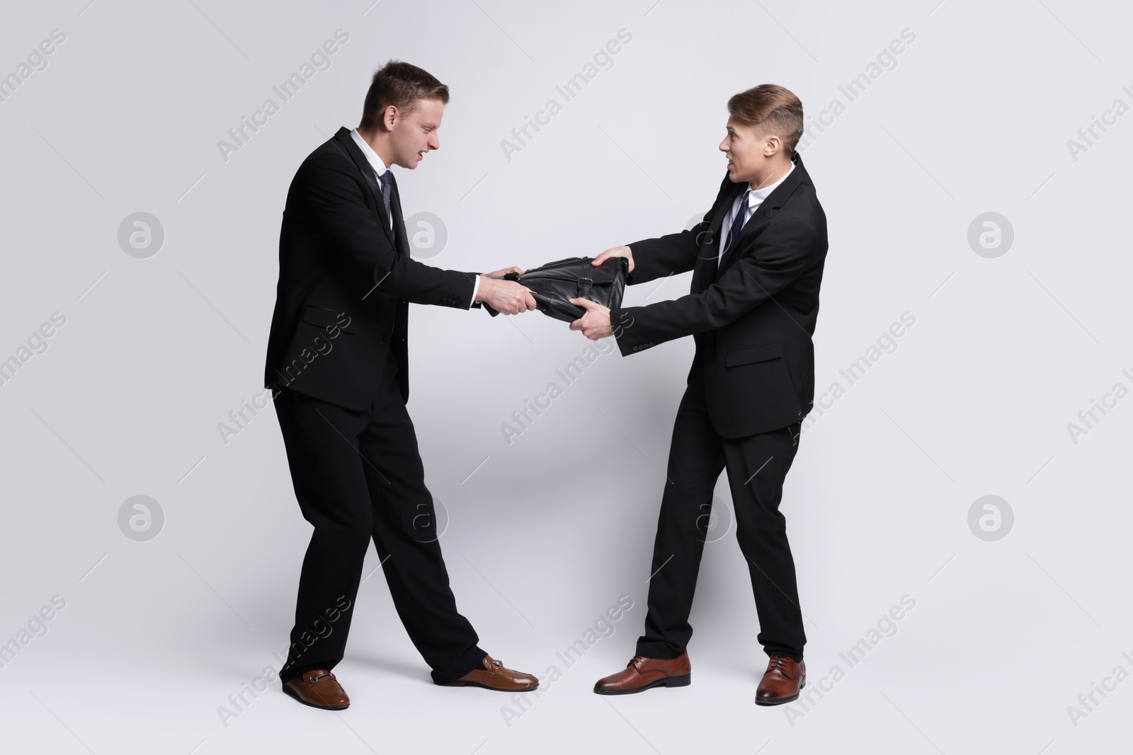 Photo of Competition concept. Businessmen pulling leather briefcase on grey background