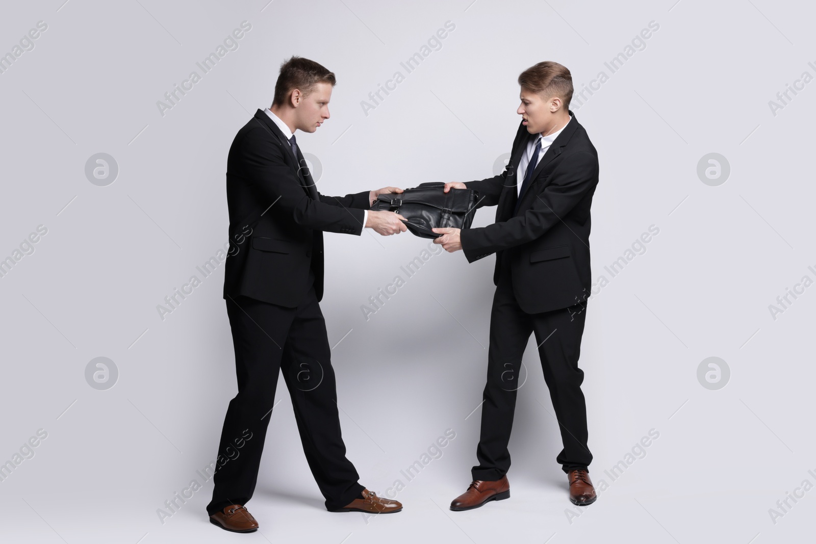 Photo of Competition concept. Businessmen pulling leather briefcase on grey background