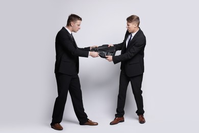 Competition concept. Businessmen pulling leather briefcase on grey background