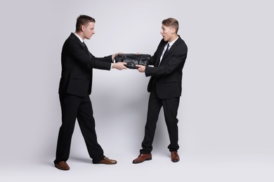 Photo of Competition concept. Businessmen pulling leather briefcase on grey background